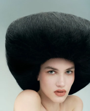 Glamour shot of a woman with bare shoulders and a striking black hairstyle against a pale blue background, fashion-forward.