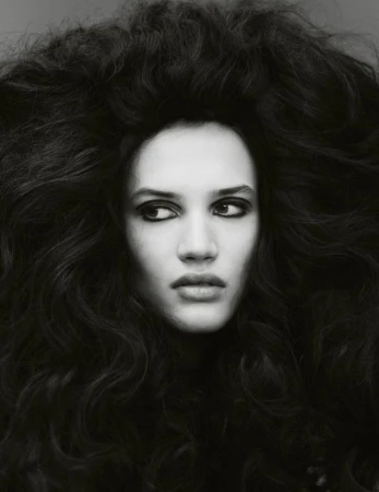 Monochrome portrait of a woman with voluminous dark wavy hair, gazing slightly to the side in a photo studio setting.