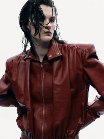 Model with wet dark hair wearing a structured red leather jacket against a neutral studio background