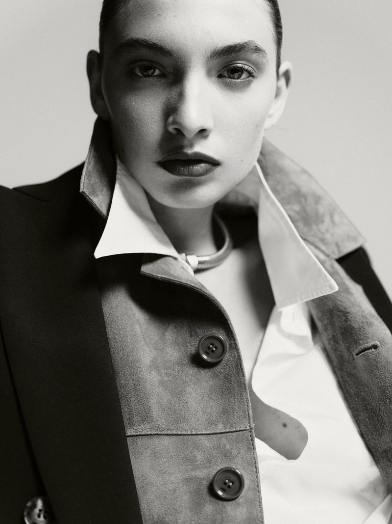 Portrait of a woman with dark hair in a short style, wearing a jacket and white shirt, looking directly at the camera with a neutral expression.
