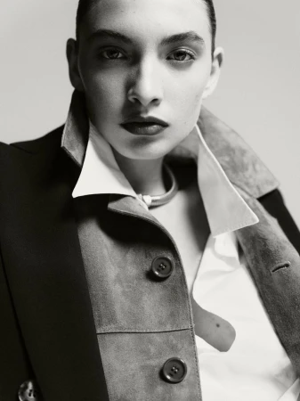 Portrait of a woman with dark hair in a short style, wearing a jacket and white shirt, looking directly at the camera with a neutral expression.