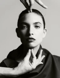 Close-up black and white portrait of a model with hands framing their face against a seamless background.