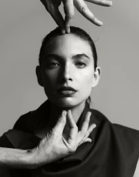 Black and white portrait of model Rolf with hands framing forehead and chin against a grey backdrop
