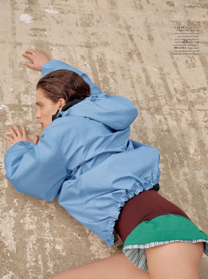 Fashion editorial shot of a woman in a blue jacket lying on a concrete surface, showcasing a modern and relaxed aesthetic.