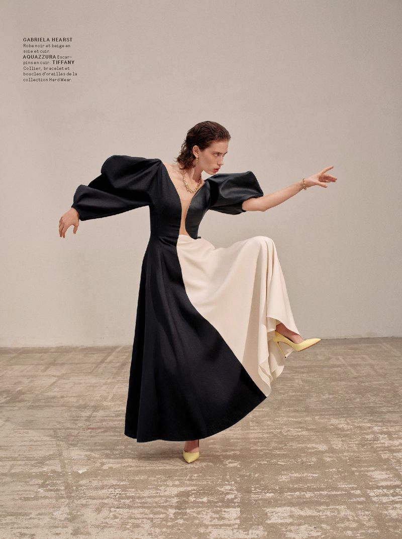 A model strikes a pose in a two-tone gown with puffy sleeves, accented by yellow heels, in a fashion forward indoor setting.