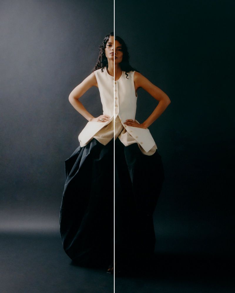 Full-length studio portrait of a woman in a beige top and black balloon skirt, striking a confident pose with hands on her waist.