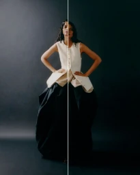 Model in a cream buttoned vest and black voluminous skirt against a split light and dark studio backdrop.