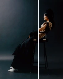 Model seated on a tall director chair wearing a long black coat against a dark studio background