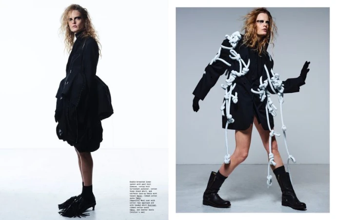 Editorial fashion shot: Woman in black jacket with decorative white rope details and black boots poses in a bright photo studio.