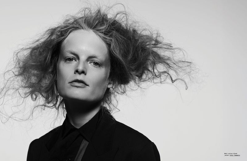 Black and white close-up portrait of a young woman with tousled hair, wearing a dark blouse against a bright white background.