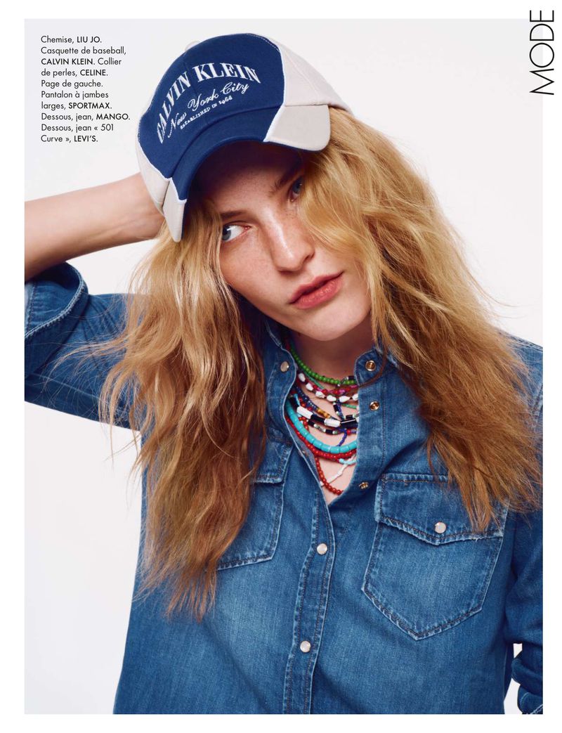 Blonde woman wears a Calvin Klein baseball cap and denim shirt with colorful beaded necklaces in a fashion editorial shot indoors.