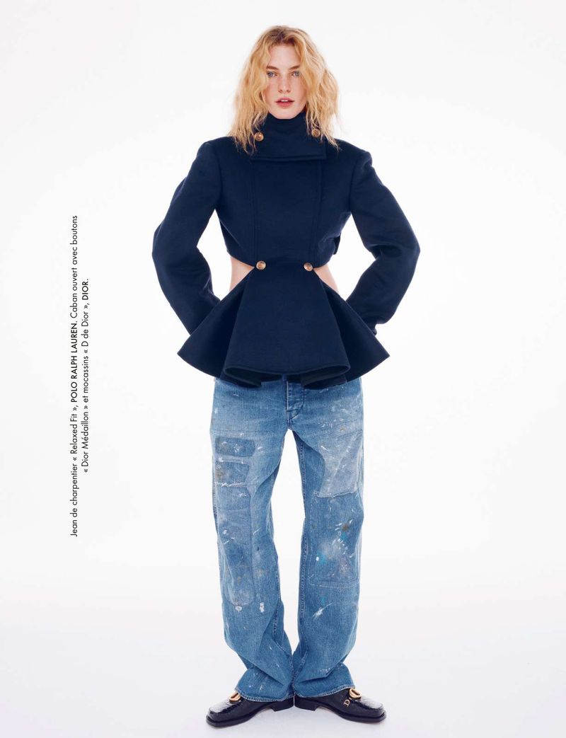 Fashion shot of a young adult woman posing in a black jacket with cut-outs, wide-leg jeans, and loafers against a white backdrop. 