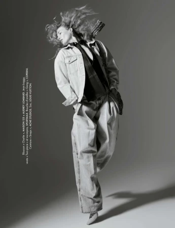 Monochrome studio shot of a stylish young woman in an unbuttoned denim jacket and wide-leg jeans, captured in mid-movement with flowing hair.