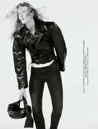 Monochrome fashion shot of a blonde adult woman wearing a leather jacket and jeans, holding a helmet, against a white background.