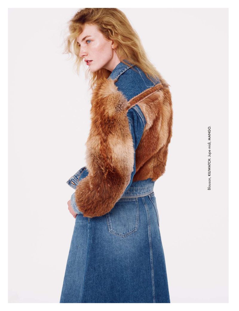 Fashion editorial shot of a blonde adult woman wearing a denim skirt and a denim jacket with fur accents against a white backdrop.