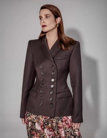 Cobie Smulders wearing a dark double-breasted blazer and floral skirt against a neutral background.