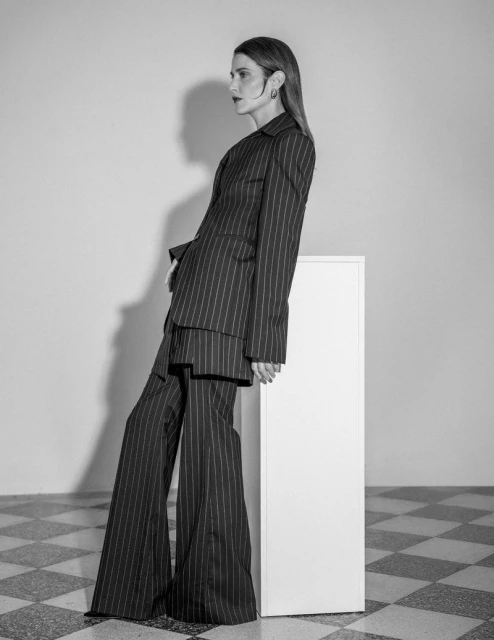 Black and white portrait of a woman in a pinstripe suit leaning against a white column in front of a checkerboard tiled floor.