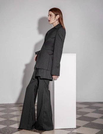 Cobie Smulders leaning against a white pedestal wearing a pinstripe pantsuit with wide-leg trousers
