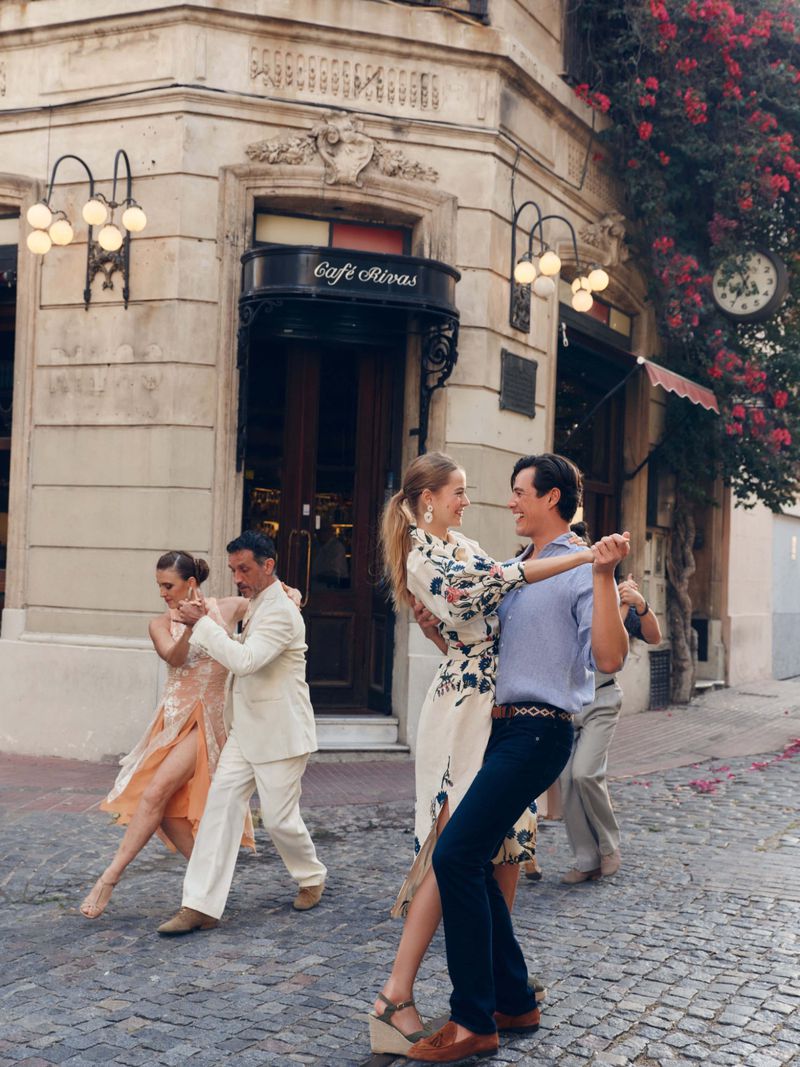 Two couples dancing tango on a cobblestone street near Café Rivas in Buenos Aires, Argentina, with vintage architecture and outdoor lighting.