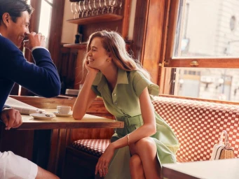 Man and woman seated together in a café with checkerboard booth seating, smiling during a lifestyle shoot for Tuckernuck.