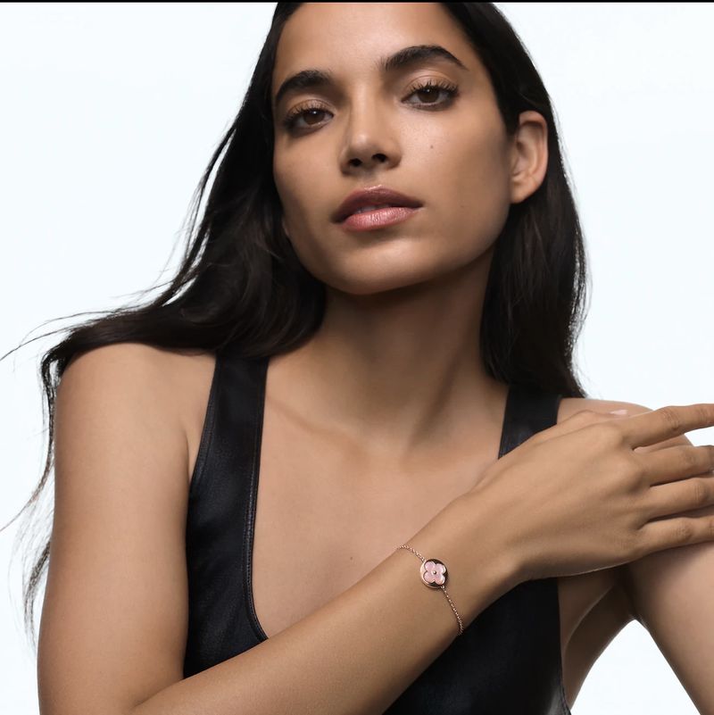 Portrait of woman wearing a black top and a rose gold bracelet with a pink flower charm on a white background in a studio setting.