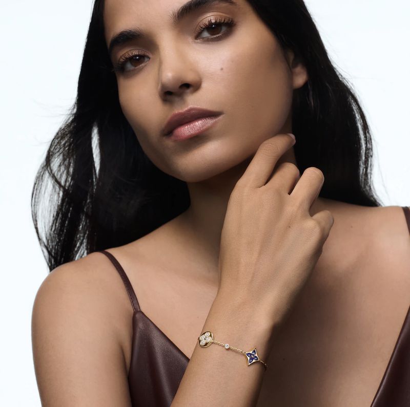 Elegant woman showcasing a gold bracelet with floral motifs against a bright background, highlighting the beauty product and jewelry.