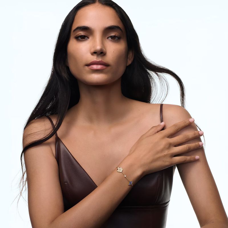 A woman wearing a brown top and bracelet in a studio with a white background, close-up.