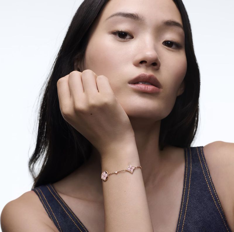 Close-up of a model wearing a gold bracelet with floral and circular charms, against a white background in a studio setting.