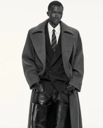 Man wearing a grey wool coat, dark suit jacket, white shirt, striped tie, and leather gloves against a plain background