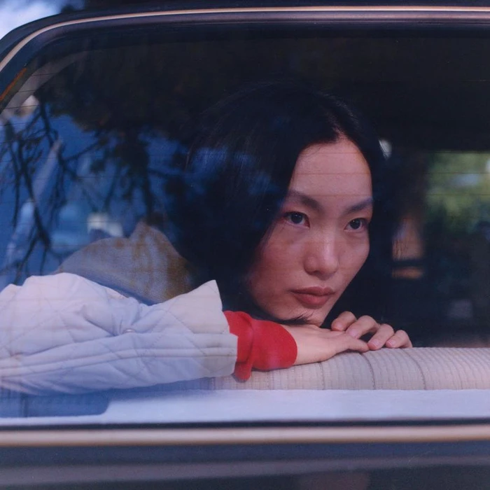 Asian woman resting her chin on her hands while looking out from inside a car window
