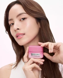 Woman holding a pink jar of L'Oreal Paris Glycolic Bright cream against a clean white background.