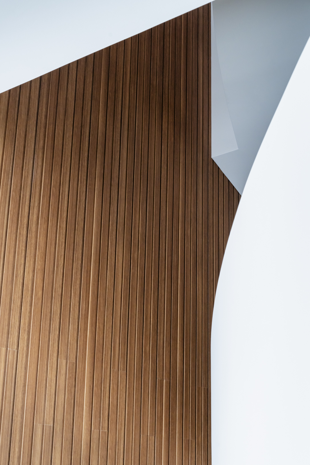 Close-up shot of a brown wooden wall with vertical planks alongside a section of a curved white wall, creating a minimalist aesthetic.