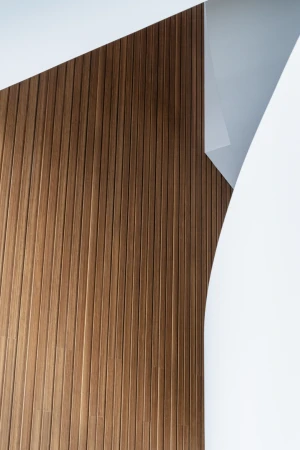 Close-up shot of a brown wooden wall with vertical planks alongside a section of a curved white wall, creating a minimalist aesthetic.