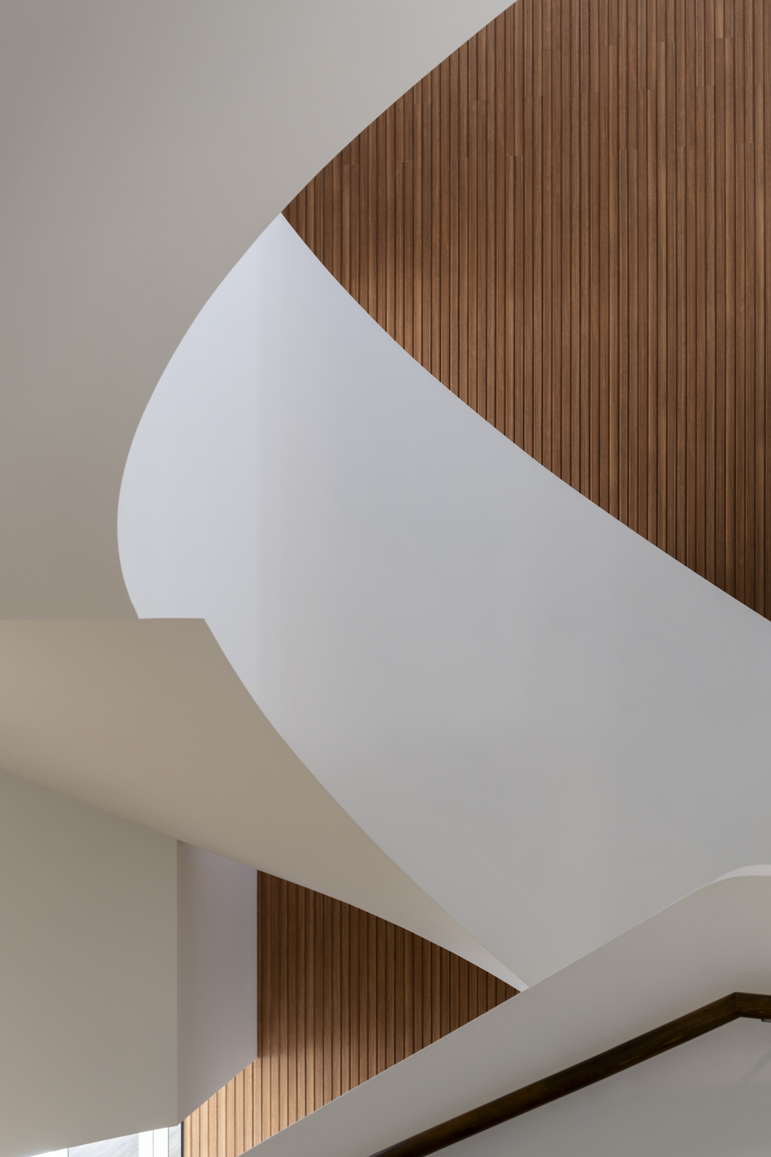 Abstract architectural detail of a modern interior featuring curved white walls and wood paneling, creating a minimalist and geometric design.