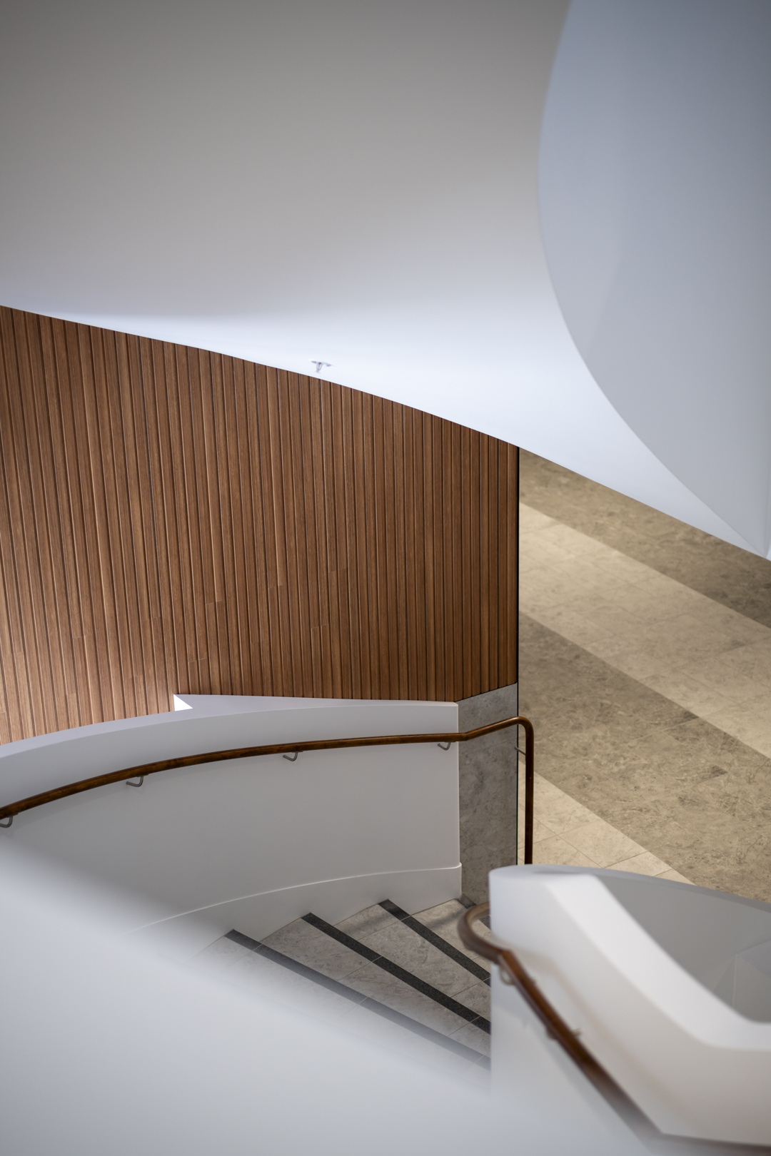 Architectural shot of a modern staircase with white railings, wood paneling, and a marble floor creating a clean, geometric composition.