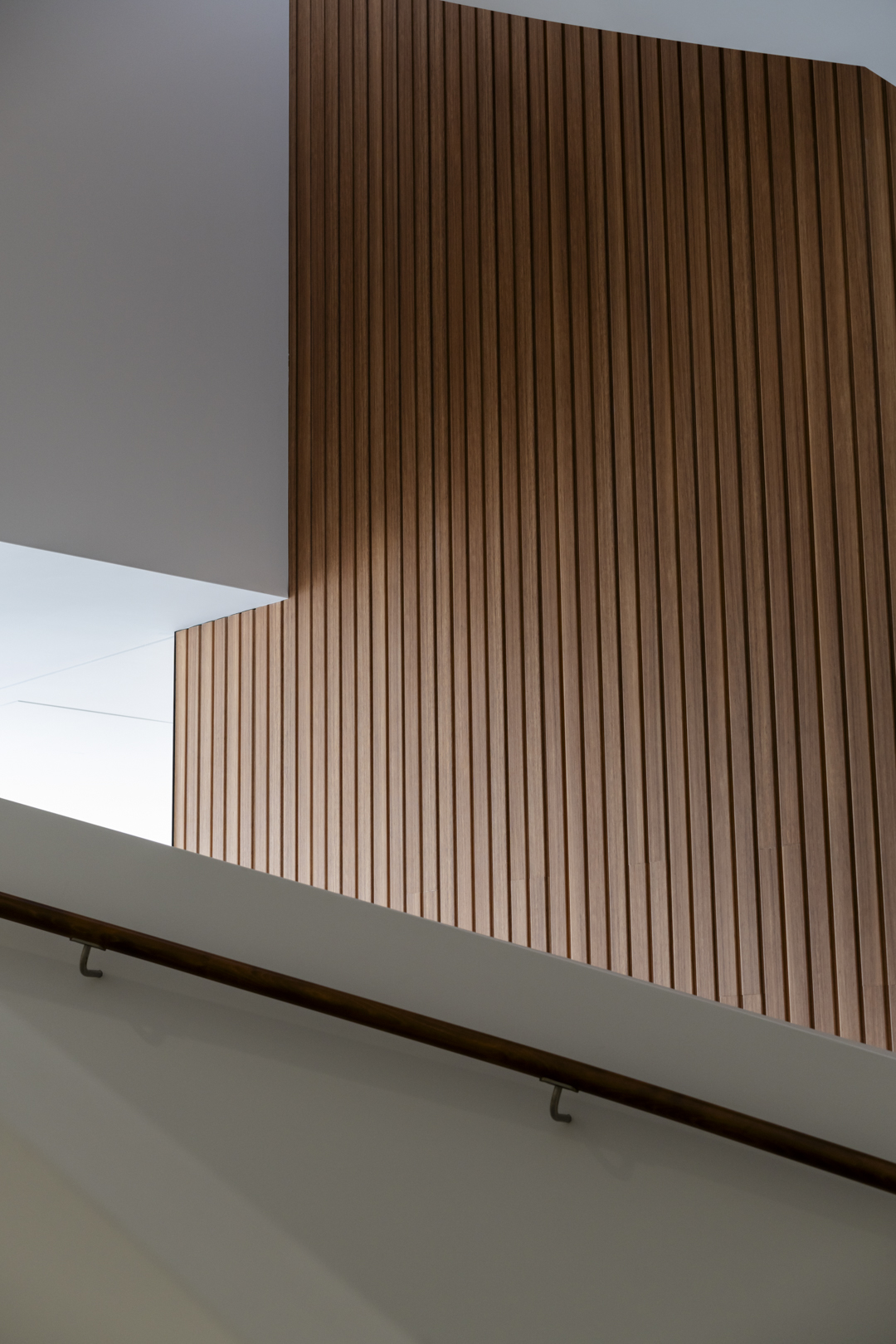 Abstract view of modern architectural wood paneling with a railing, white walls, and ambient lighting for interior design.