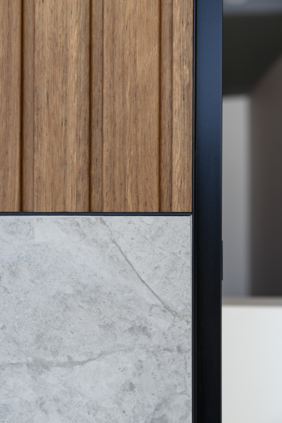 Close-up of interior wall with light wood paneling, grey stone tile, and a dark metal frame creating a modern architectural detail.