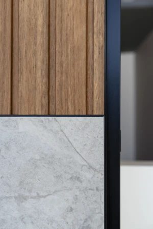 Close-up of interior wall with light wood paneling, grey stone tile, and a dark metal frame creating a modern architectural detail.