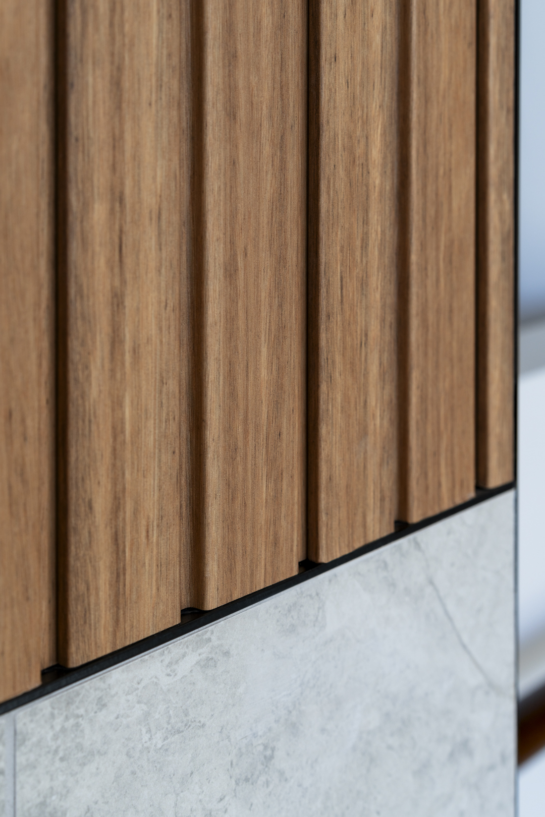 Close-up of a panel featuring vertical wood slats above a concrete slab wall, highlighting the texture and joinery.
