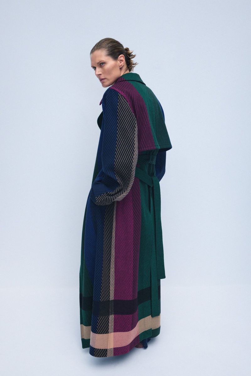 A person is seen from the back, standing in a photo studio wearing a colorful patterned overcoat and looking over their shoulder.