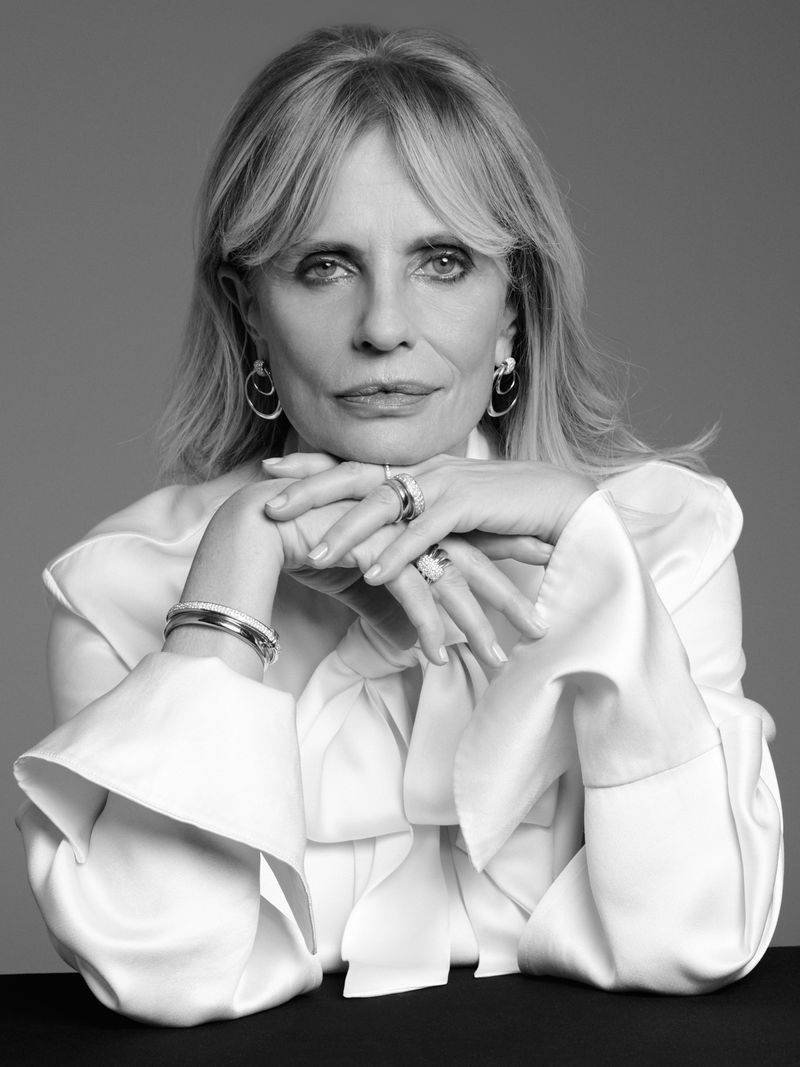 Portrait of mature woman with hands under chin, wearing white blouse and jewelry in a studio setting; monochromatic image.
