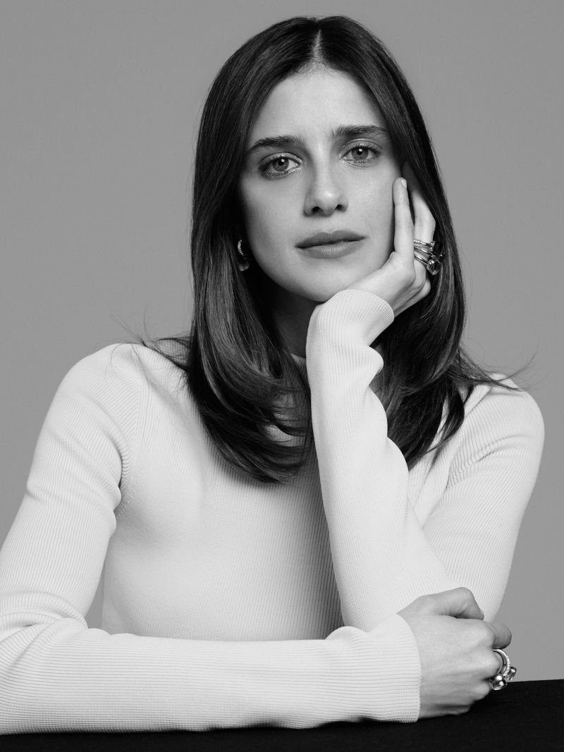 Monochrome portrait of a middle-aged woman with long brown hair wearing a cream turtleneck, posing with her hand against her face.