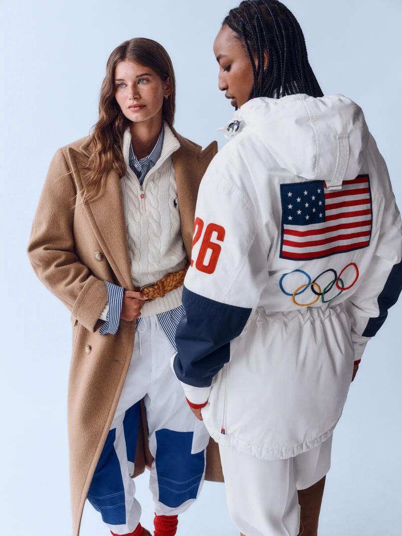 Two models in Ralph Lauren Olympic collection: one in a beige coat and the other in a white jacket with American flag and Olympic rings.