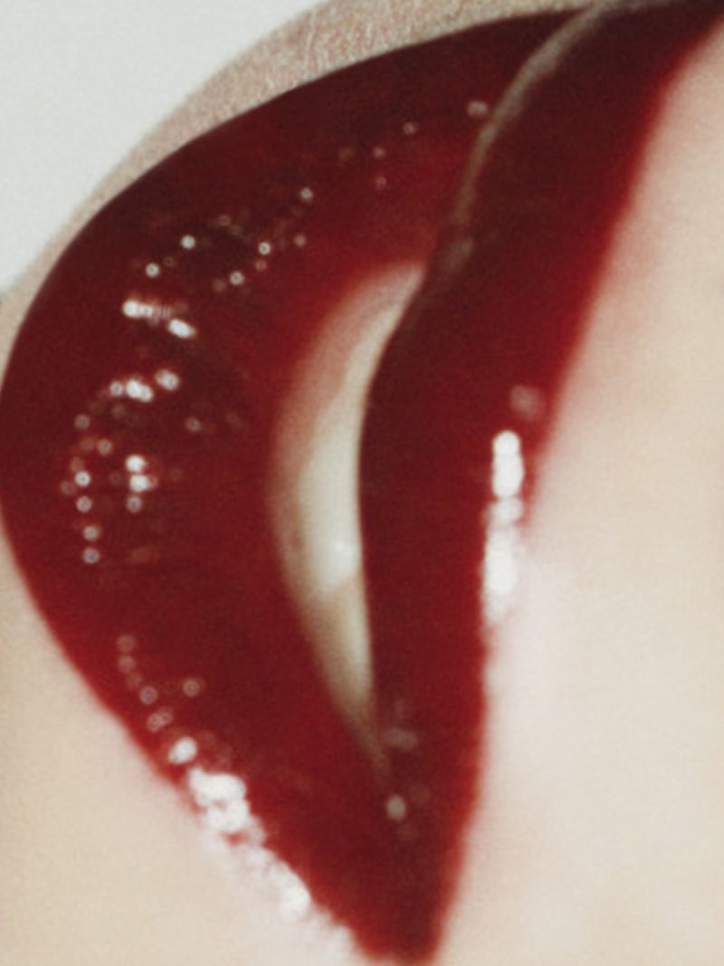 Macro shot of a woman's red glossy lips, showing detail and texture. Close-up captures the shine and curvature of the lip, beauty concept.