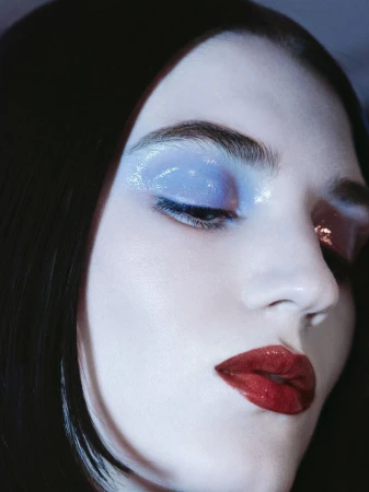 Close-up portrait of a woman with blue eye makeup and glossy red lips, highlighting beauty and cosmetic application in a studio setting.