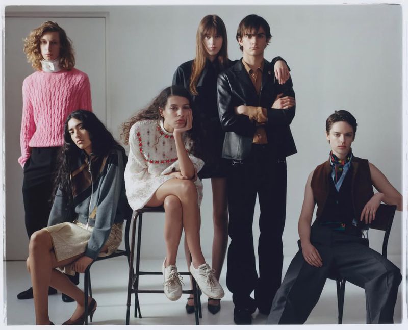 Group fashion shot of six people wearing different outfits in front of a white wall, showcasing diverse styles and a collaborative presentation.