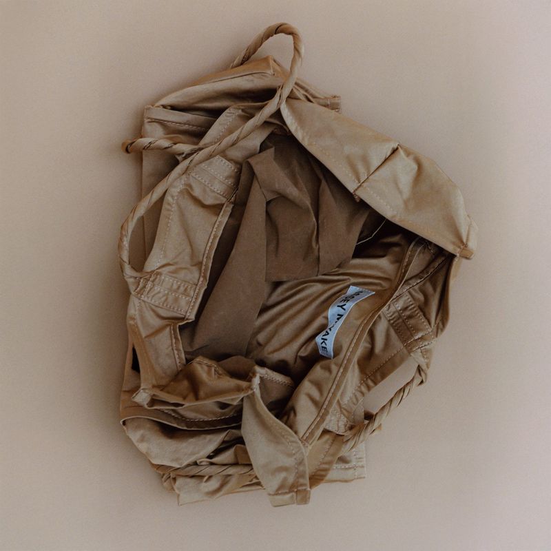 Tan-colored garment or cloth, possibly a dress or top, with string straps and visible label, on a beige background.