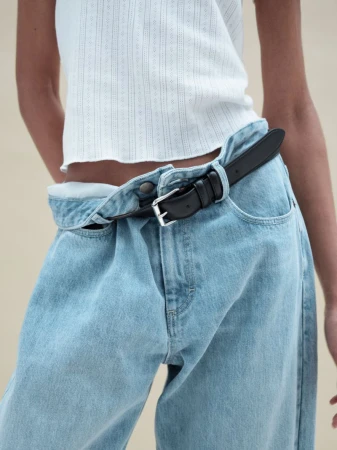 Model wearing a white ribbed top and light wash denim jeans with a black belt against a neutral background