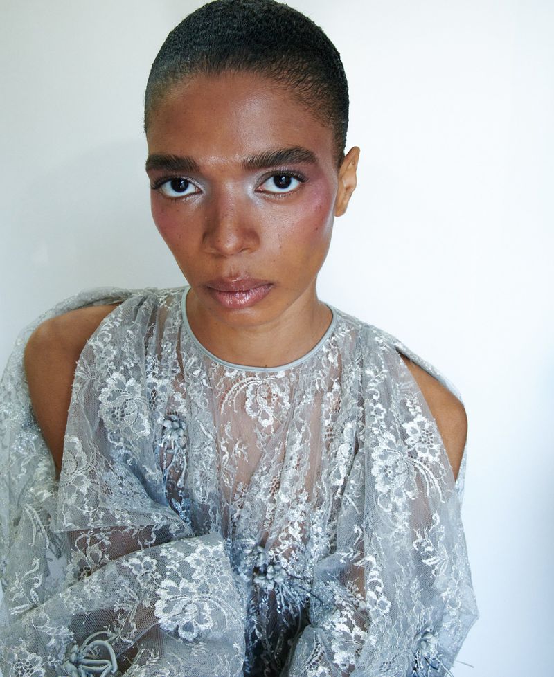 Close-up portrait of an adult female with short hair wearing a lace top with open shoulders, against a white backdrop.