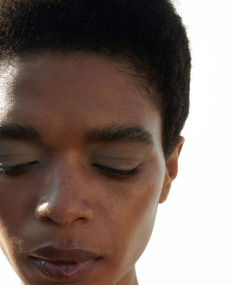 Close-up portrait of a woman with dark hair and a serene expression, eyes closed, in bright lighting against a plain white background.